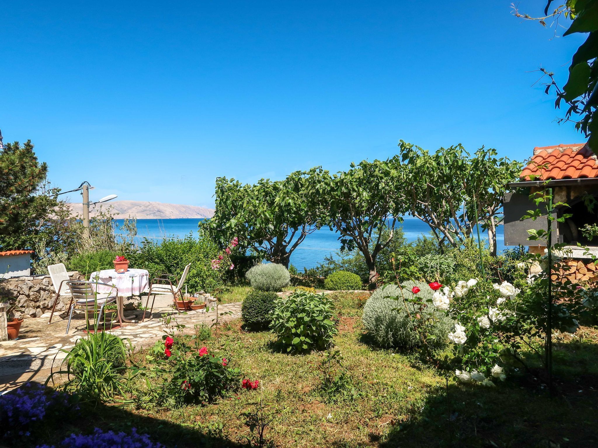 Ein Garten mit Terrasse, einer Steinmauer und Blick aufs Meer.