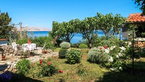 A garden with a patio area, a stone wall, and a view of the sea.