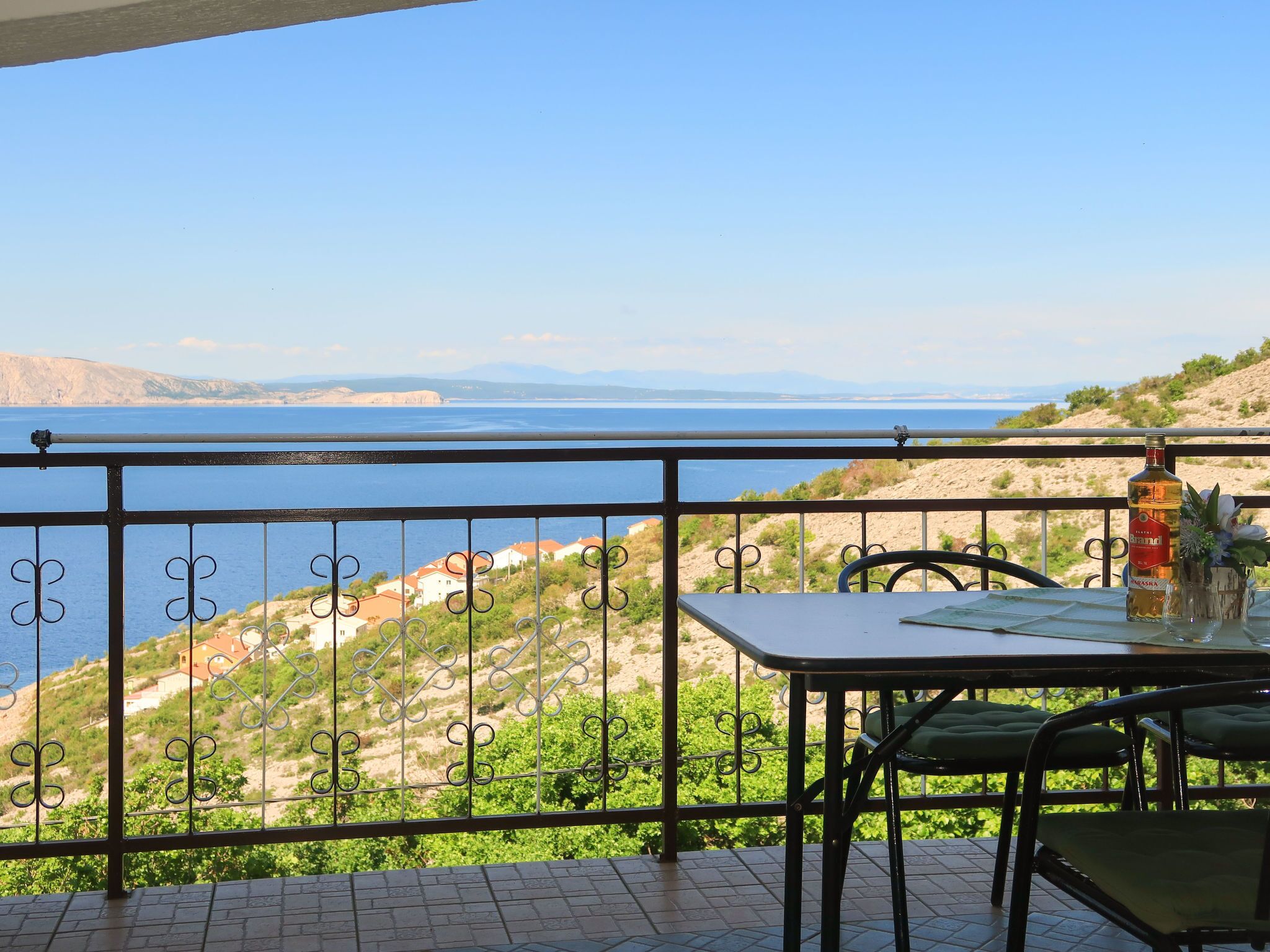 A balcony with a table and chairs overlooking a coastal landscape with houses and a body of water.