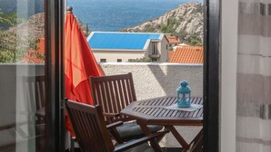 Un balcon avec une table et des chaises, donnant sur un paysage côtier avec des bâtiments et un terrain rocheux.