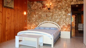 A bedroom with a stone wall, wooden ceiling, a bed with a white headboard, a bedside table, and a bench. - Apartment Visnja by Interhome (Crikvenica/Jadranovo)