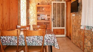 A wooden dining area with a stone wall, a wooden cabinet with kitchenware, and a television mounted on the wall. - Apartment Visnja by Interhome (Crikvenica/Jadranovo)