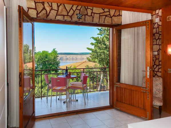 A balcony with a table and chairs, a view of a lake, and a stone wall.