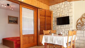 A dining area with a table set for four, wooden chairs, a television mounted on the wall, and a stone-patterned wall behind the table.