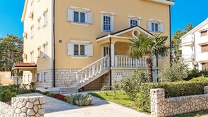 A two-story building with a yellow facade, multiple windows with shutters, a central entrance with a staircase, and a stone wall surrounding the property. - Villa Anna by Interhome (Crikvenica/Jadranovo)