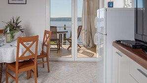 Ein Essbereich mit einem Tisch für zwei Personen, Holzstühlen, einer weißen Tischdecke und Meerblick durch eine Glastür.