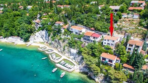 Luftaufnahme einer Küstenstadt mit Häusern, einem Jachthafen und klarem, türkisblauem Wasser.
