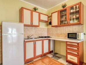 A compact kitchen with a refrigerator, stove, microwave, and wooden cabinets. - Apartment Nikol by Interhome (Crikvenica)