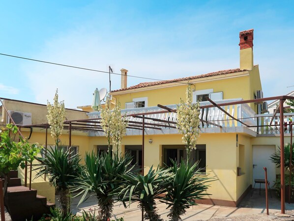 A yellow building with a red-tiled roof, a balcony with a white railing, and several potted plants in the foreground. - Vacation home Mateja by Interhome (Krk/Krk)