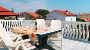 Une terrasse avec une table dressée pour deux personnes, des chaises blanches et une balustrade blanche.