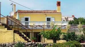 Un bâtiment jaune avec un toit recouvert de tuiles rouges, un balcon blanc et un escalier en pierre.
