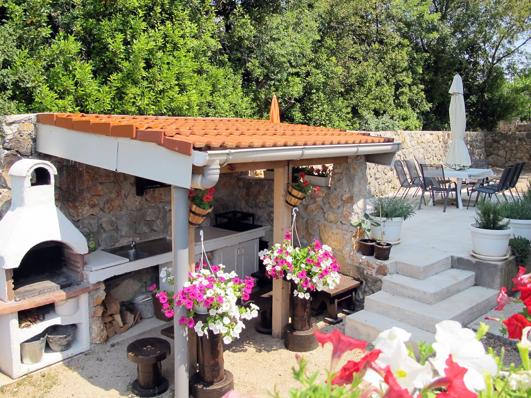 An outdoor kitchen area with a stone wall, a brick oven, and hanging flower baskets.