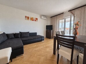 A modern living room with a sofa, a dining table with chairs, a flat-screen TV, and a decorative vase.