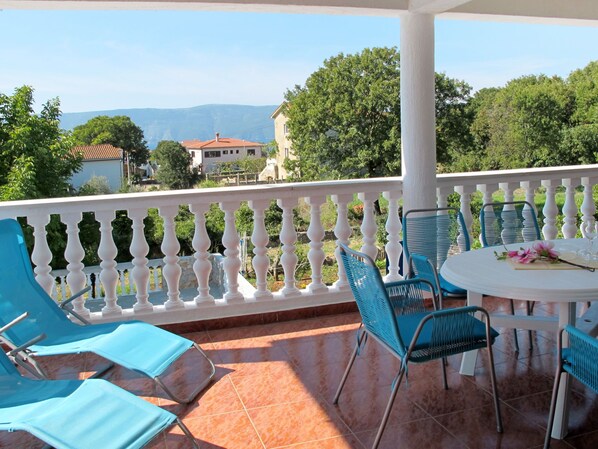 A balcony with blue chairs and a table, overlooking a scenic view of trees and buildings.