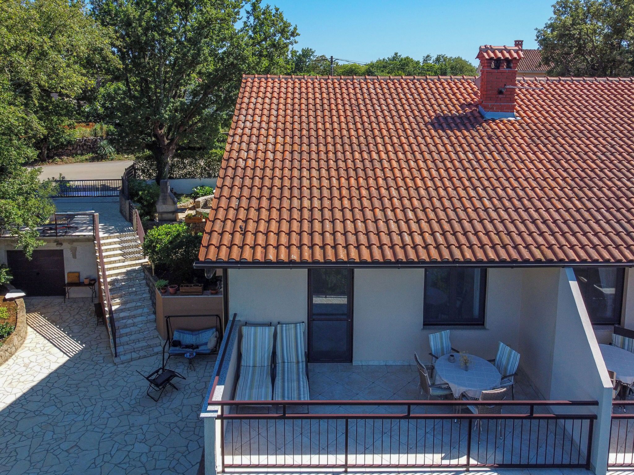 Ein zweistöckiges Haus mit einem Ziegeldach, einem Balkon mit Gartenmöbeln und einer Steinmauer.