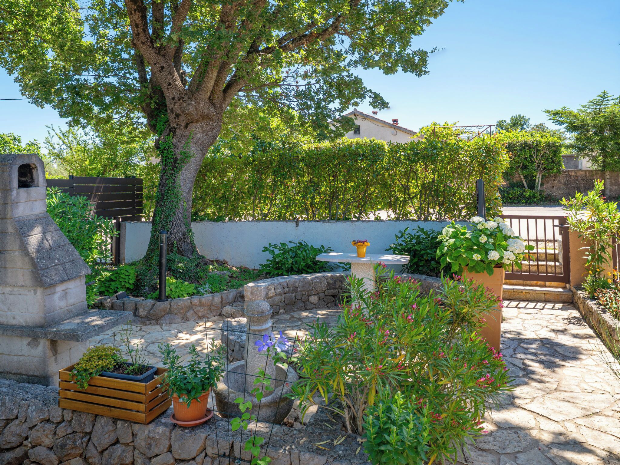 A stone patio with a stone bench, a small table with a yellow vase, and a variety of potted plants.