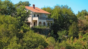 Un bâtiment à deux étages, surmonté d’un toit recouvert de tuiles rouges, et entouré d’une végétation luxuriante.