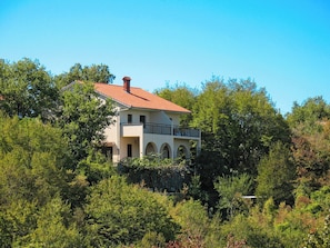 A two-story building with a red-tiled roof, surrounded by dense greenery.
