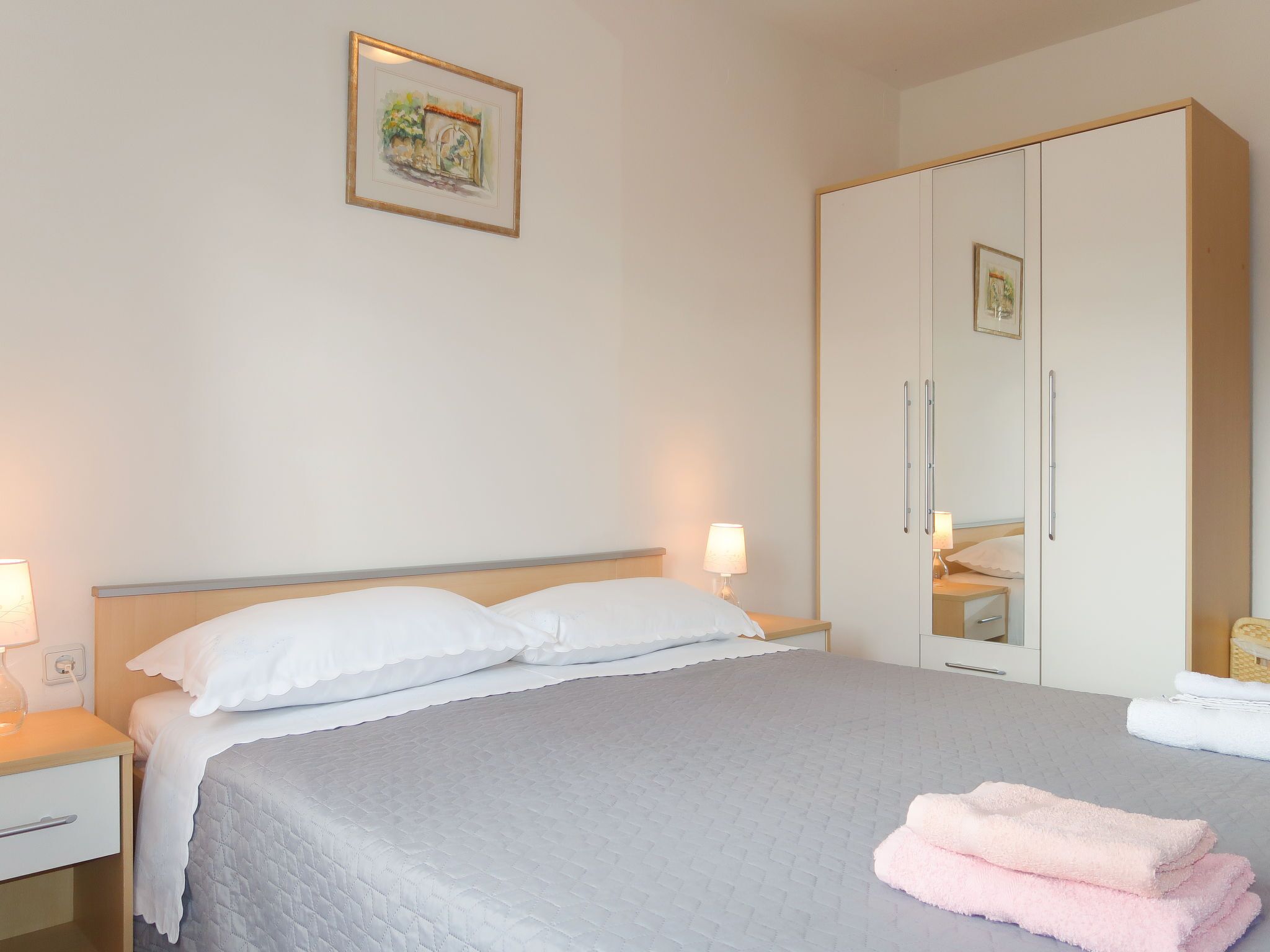 A hotel room with a bed, bedside lamps, a wardrobe, and a framed picture on the wall.