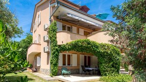 Ein zweigeschossiges Gebäude mit überdachter Terrasse, Gartenmöbeln und üppiger Bepflanzung.