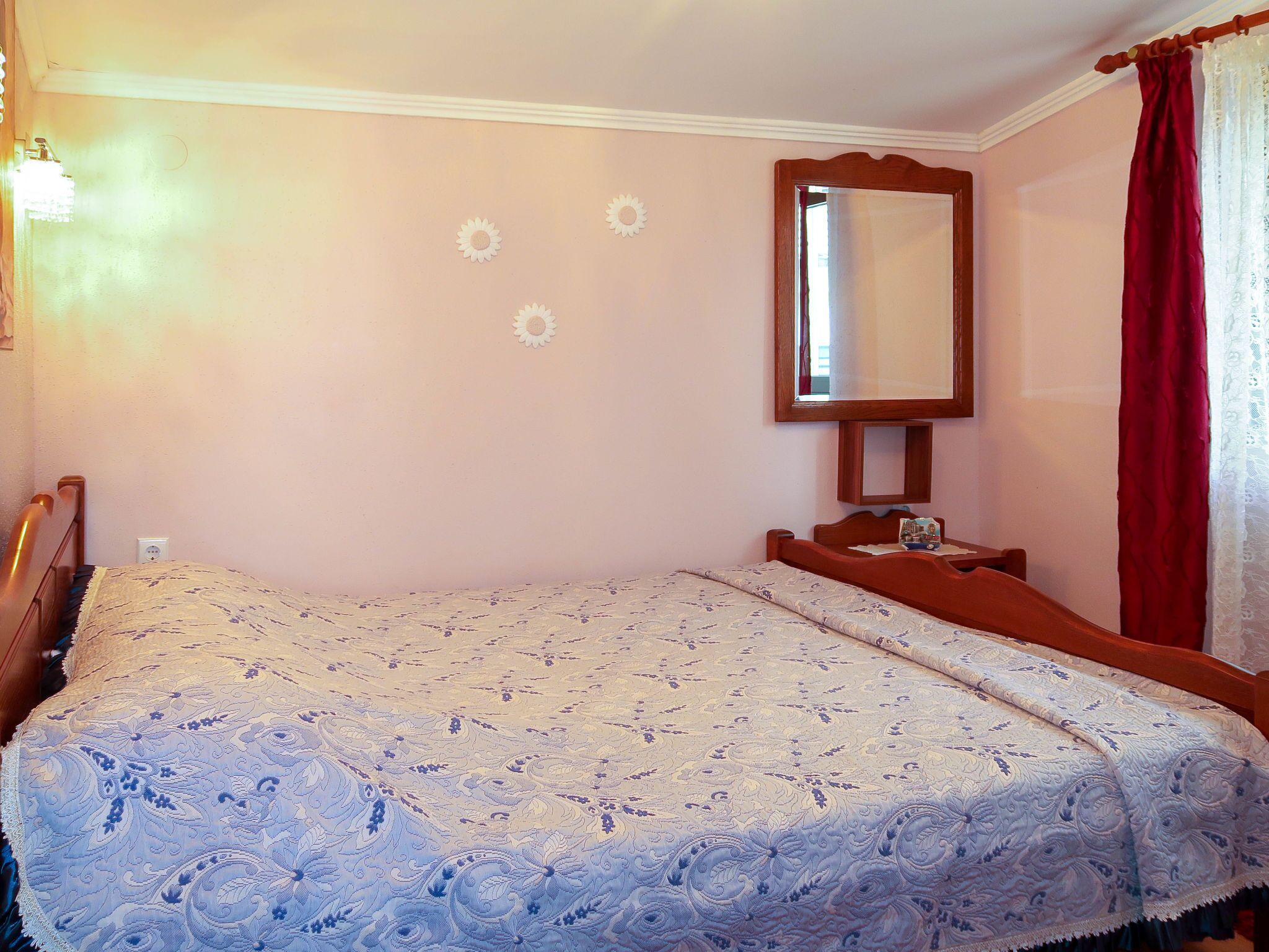 Ein Schlafzimmer mit Bett, Nachttisch, Spiegel und einem roten Vorhang.