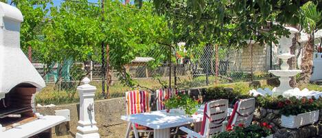 An outdoor patio with a grill, white table and chairs, and potted plants.