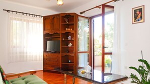 Un salon avec un canapé vert, un meuble de rangement en bois pour les appareils électroniques et une table basse avec un plateau en verre.