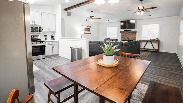 A spacious kitchen with white cabinets, a wooden dining table, and a ceiling fan.