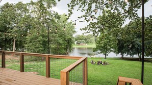 A wooden deck overlooking a grassy area with a pond and trees.
