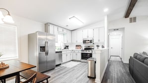 A modern kitchen with stainless steel appliances, white cabinetry, and a grey sofa in the living area.