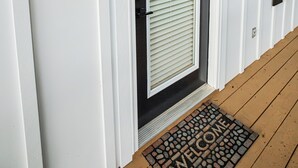 A white door with a black frame, a lit wall lantern, and a welcome mat.