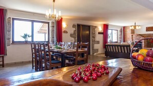 Un coin repas avec une table en bois dressée pour le repas, un lustre et un panier de fruits posé sur la table.