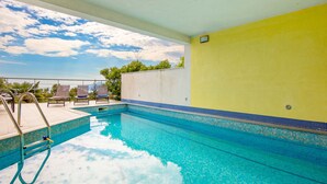 Une piscine à l’eau d’un bleu cristallin, un mur jaune et une vue sur le ciel.
