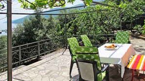 A terrace with a table and chairs, overlooking a body of water and greenery.
