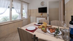 A dining area with a table set for two, a clock on the wall, and a TV above the counter.