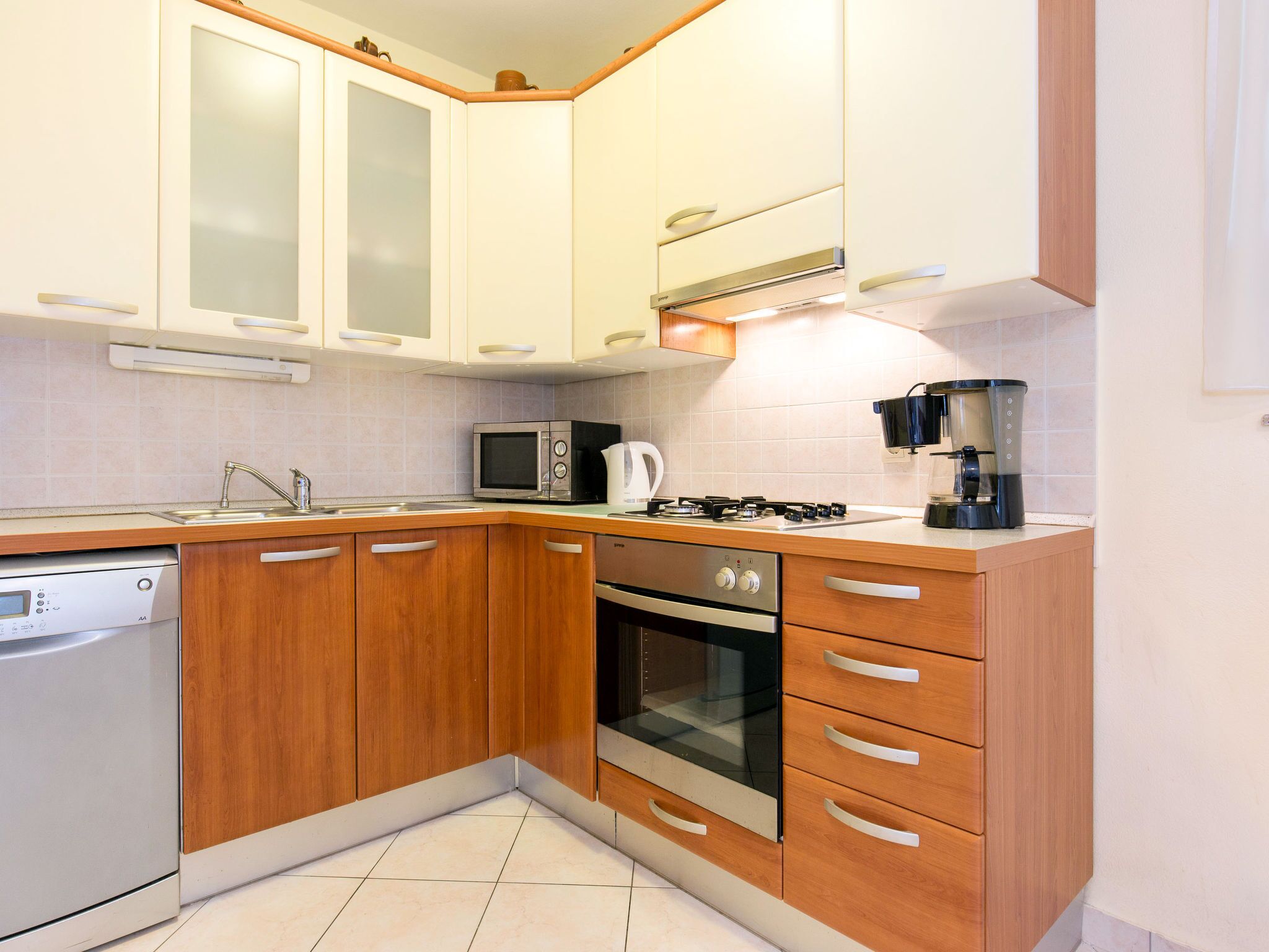 Une cuisine moderne avec des meubles en bois, un four à micro-ondes encastré, une cuisinière à gaz et une machine à café.