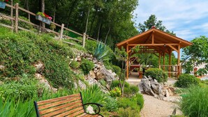 Un banc en bois doté d’une structure métallique, une pergola en bois et un chemin de gravier dans un jardin aménagé.