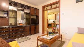 Un salon comprenant un canapé, une table basse et un téléviseur. Il y a également un coin cuisine avec des placards et une table à manger.