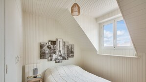 A bedroom with a sloped ceiling, a bed, a nightstand, a lamp, and a window with a view of the sky. - 190m from the beach, downtown, house for 8 (Pléneuf-Val-André)