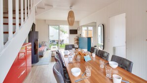 A dining area with a long wooden table set for six, surrounded by chairs. A staircase with white railings is visible on the left. - 190m from the beach, downtown, house for 8 (Pléneuf-Val-André)