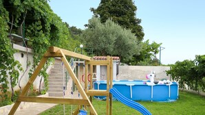 Ein Schaukelstuhl aus Holz mit einer Rutsche, ein kleiner Pool mit einem Spielpferd und eine Steinmauer in einem Garten.