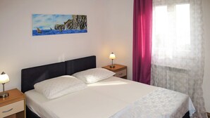 A neatly made bed with a white and patterned bedspread, a black headboard, and a nightstand with a lamp. - Princip by Interhome (Rabac)