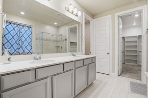 A bathroom with a large mirror, two sinks, and a walk-in shower.