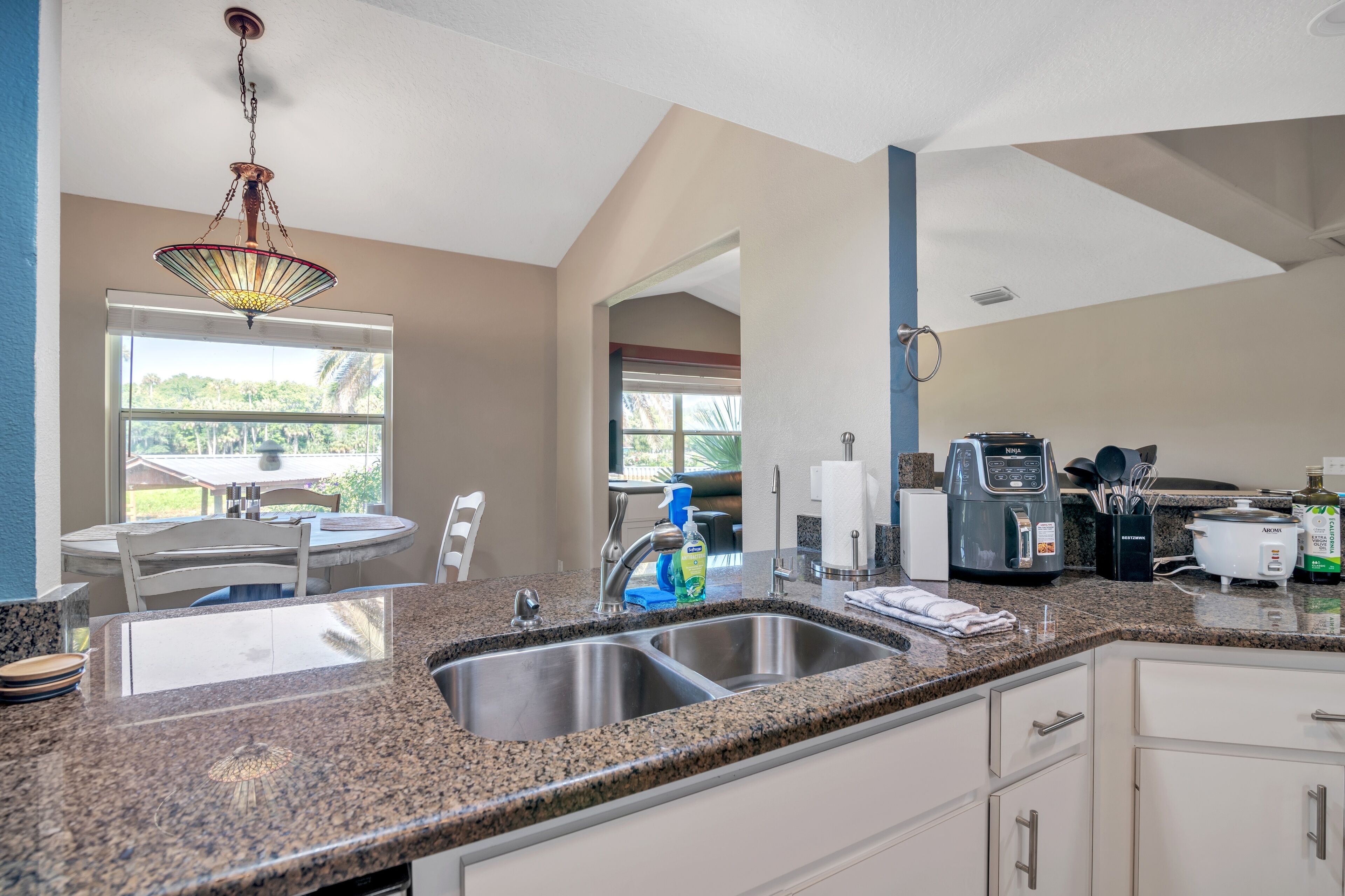 A kitchen with granite countertops, stainless steel sinks, and a hanging light fixture.