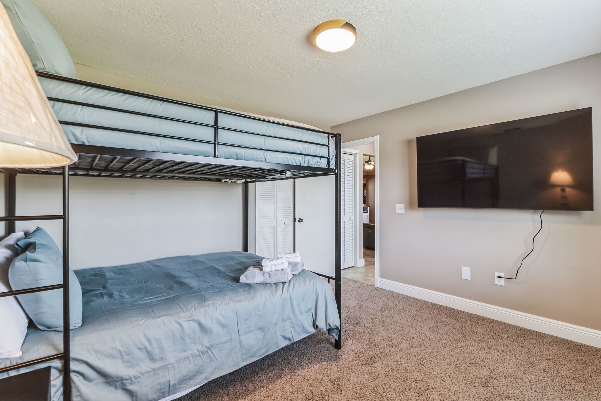 A bunk bed room with a TV mounted on the wall, carpeted floor, and a door leading to another room.