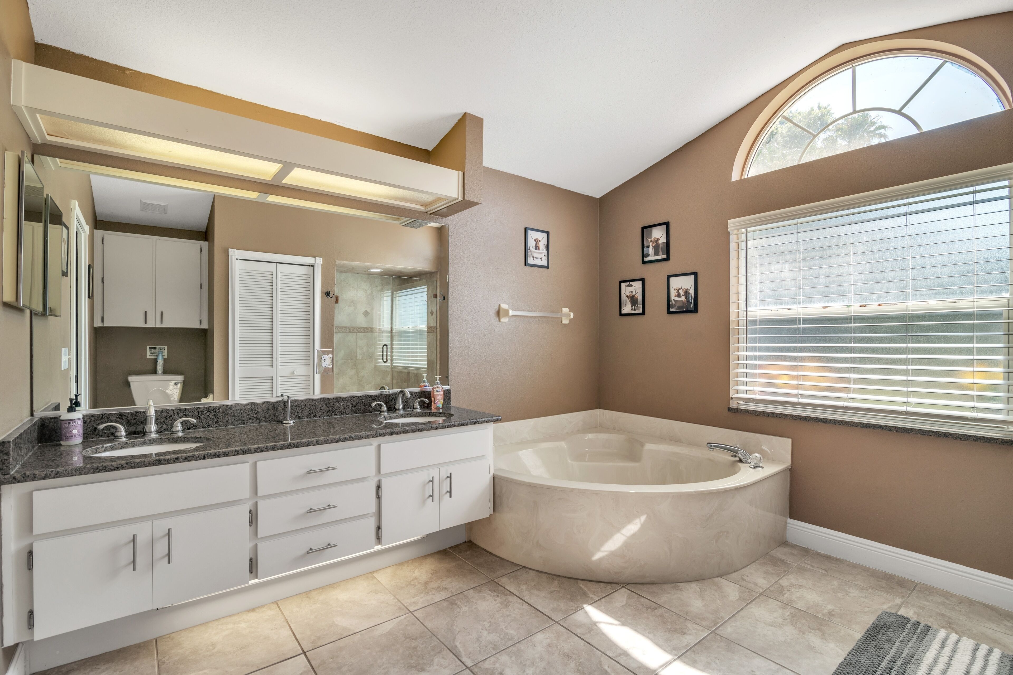 Ein modernes Badezimmer mit einer großen Badewanne, einem Waschtisch mit Spiegel und einem Fenster mit Jalousien.