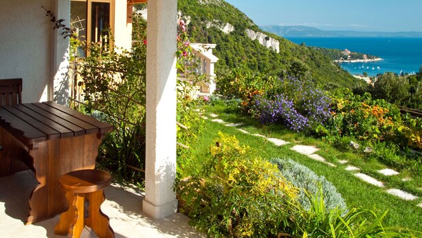 A covered outdoor area with a wooden bench and table, surrounded by lush greenery and a view of the sea and cliffs. - Princip by Interhome (Rabac)