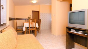 A living room with a sofa, a dining table with chairs, a television on a stand, and a door leading to another room. - Princip by Interhome (Rabac)