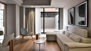 Ein modernes Wohnzimmer mit einer Couch, einem Sessel, einem Glastisch und Blick auf einen Balkon.
