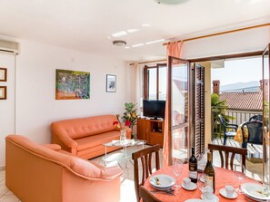 Relax in this open-plan living space with a comfortable sofa, dining table for two, and a TV mounted on a cabinet.